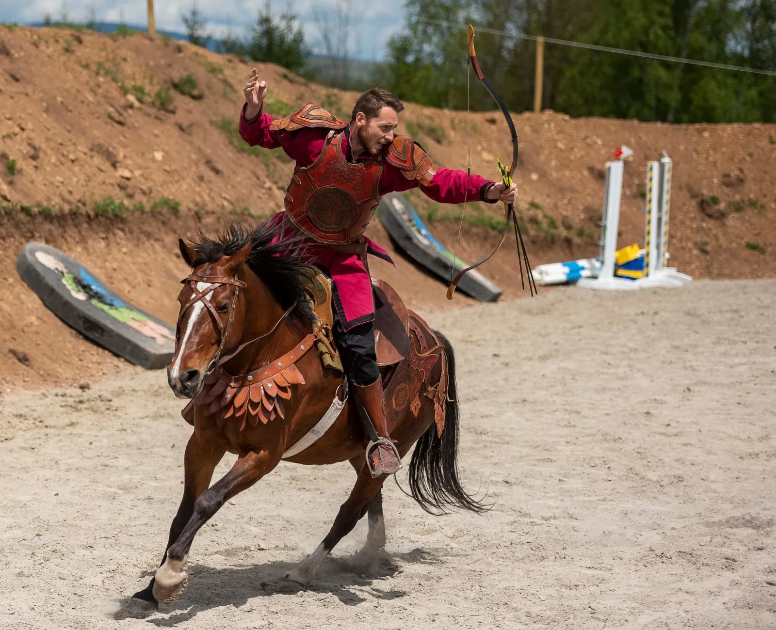 Un arcaș ecvestru în costum istoric galopează pe o pistă de nisip.