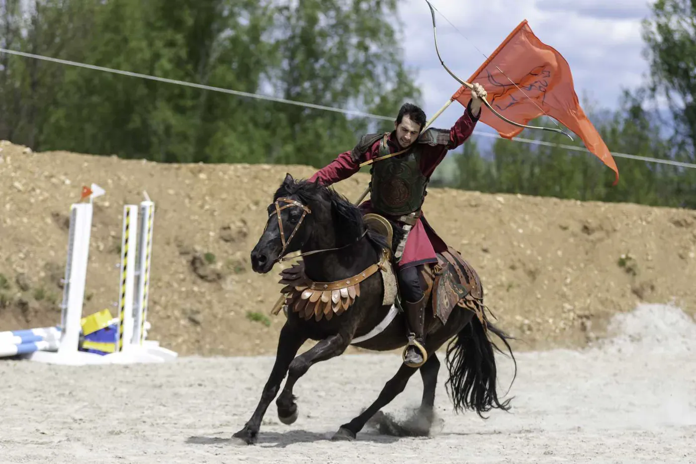 Un călăreț în costum vișiniu galopează pe un cal negru.